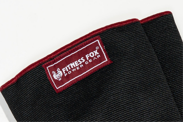 “Lifestyle image of Fitness Fox burgundy knee sleeves packed in a gym bag beside lifting belt and wrist wraps for ready training kit.”